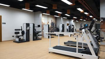 A gym with various exercise equipment, including treadmills and weight machines, and a wooden floor.