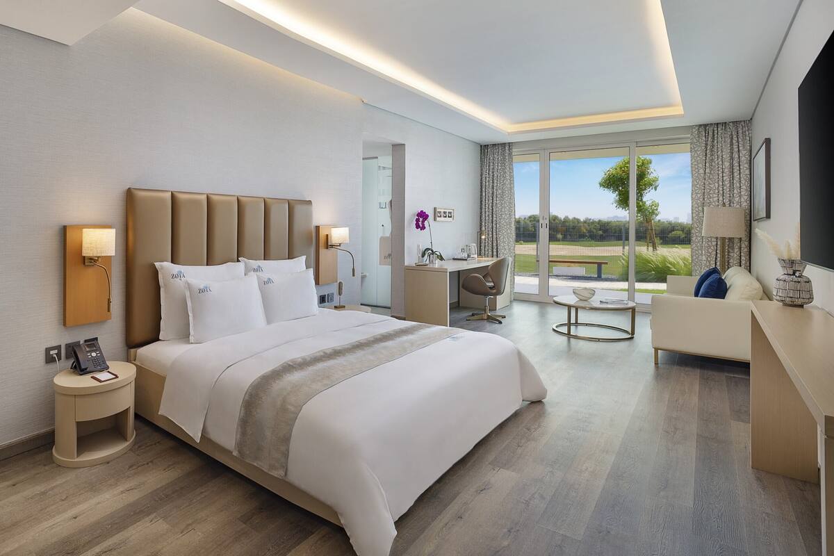 A modern hotel room with a large bed, a desk, and a view of the outdoors.