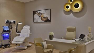 A modern dental office with a reception desk, two chairs, a computer, and a wall-mounted light fixture.