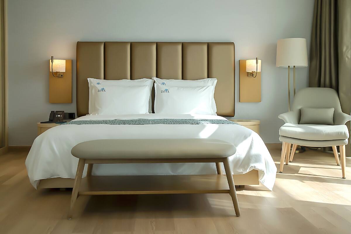 A modern hotel room with a large bed, bedside lamps, a chair, and a nightstand.
