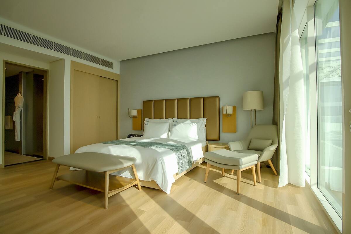 A modern hotel room with a large bed, two bedside tables, a chair, and a large window.