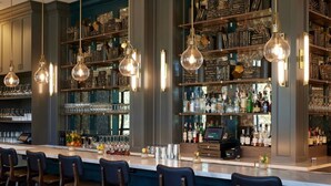Angolo bar con diverse lampade a sospensione, un bancone e scaffali pieni di bottiglie e bicchieri.