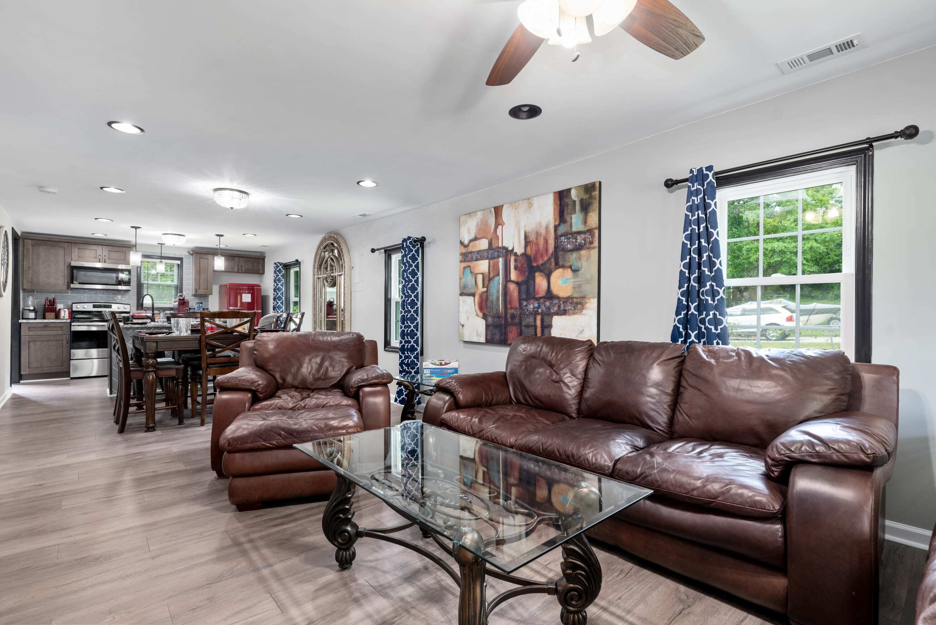 A spacious living room with leather sofas, a glass coffee table, and a dining area with a kitchen in the background.