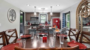 Une cuisine moderne dotée d’un îlot central, de luminaires suspendus et d’un coin repas avec des assiettes et des verres rouges.