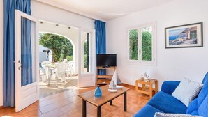 Un salon avec un canapé bleu, un téléviseur posé sur un meuble, une table basse en bois et un tableau accroché au mur.