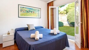 Une chambre à coucher comprenant un lit, une table de chevet, un tableau et une vue sur le jardin, accessible par une porte coulissante.