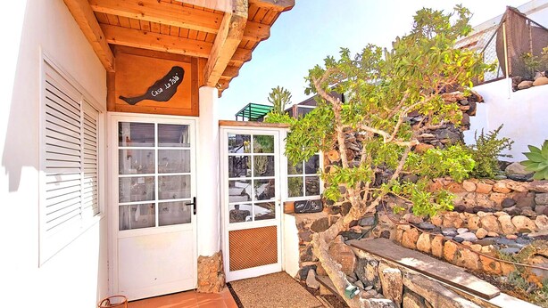 A rustic building with a wooden facade, a stone wall, and a variety of plants. - Vacation apartment CASA LA ISLA, Tarajalejo, fiber optic internet (Tarajalejo)