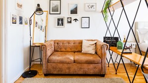 A brown leather sofa with a cushion, a standing floor lamp, and a wooden side table with a sign. - Casa da Música 5th High (Porto)