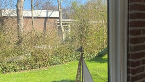 Ein Fenster mit einem Modellsegelboot auf einer Ablage, Blick auf einen grünen Garten und eine Ziegelmauer.