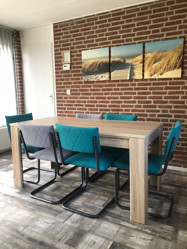 Un coin repas avec un mur en briques, une table en bois et des chaises de couleur turquoise.