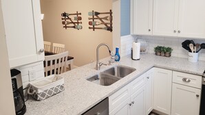 A kitchen with white cabinets, a granite countertop, a stainless steel sink, and a clock on the wall. - Ocean view flat, poolside ( ground floor). Two  bedrooms, two baths. (St. Augustine)