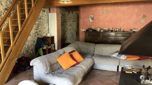 Uma sala de estar acolhedora com um sofá seccional cinza, escada de madeira e parede de pedra.