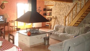 Uma sala de estar aconchegante com lareira, um sofá, uma mesa de jantar com toalha xadrez e uma escada que leva a um andar superior.