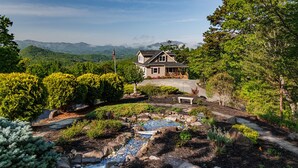 A house with a porch, surrounded by a garden with a small stream and rocks. - High View Heights stunning views and complete privacy (Bryson City)