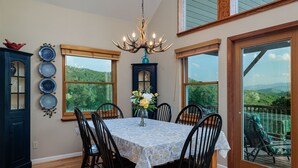 A dining area with a table set for six, surrounded by black chairs, a chandelier, and a view of a mountainous landscape through large windows. - High View Heights stunning views and complete privacy (Bryson City)
