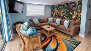 A living room with a sectional sofa, a wicker chair, and a colorful rug. - Oceanfront Tybee Cottage | Private Hot tub & Beach Access (Tybee Island)