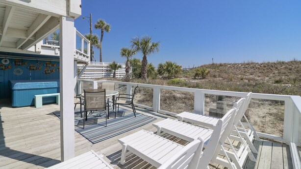 A wooden deck with white railings, a hot tub, and outdoor seating. - Oceanfront Tybee Cottage | Private Hot tub & Beach Access (Tybee Island)