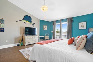 Quarto com cama grande, televisão, ventilador de teto e vista para o exterior.