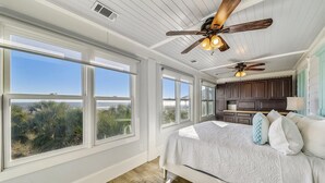 Un dormitorio con una cama grande, dos ventiladores de techo y vistas a la playa a través de amplias ventanas.