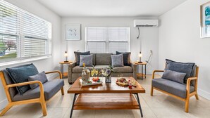 A modern living room with a sofa, two armchairs, a coffee table with food and drinks, and a window with blinds. - Frenchy’s Cottage 480 in Clearwater Beach (Clearwater Beach)