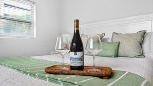 A bed with a green and white striped blanket, a bottle of Pinot Noir wine, and two empty wine glasses on a wooden tray. - Frenchy’s Cottage 480 in Clearwater Beach (Clearwater Beach)