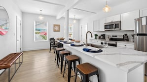 A modern kitchen with white cabinetry, a large island with stools, stainless steel appliances, and pendant lighting.