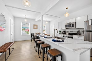 Une cuisine moderne avec des meubles blancs, un grand îlot central doté de tabourets, des appareils en acier inoxydable et un éclairage suspendu.