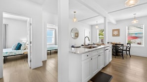 A modern kitchen with white cabinetry, a dining area with a table and chairs, and a view of the outdoors through a window.