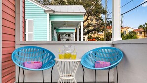 Ein Balkon mit zwei blauen Stühlen, einem weißen Tisch und einer Karaffe mit Getränken.