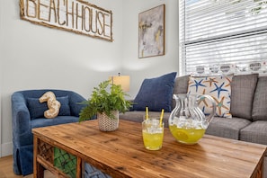 A living room with a blue sofa, a wooden coffee table, a glass pitcher, and a potted plant.