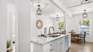 A modern kitchen with white cabinetry, a marble countertop, a sink, and pendant lighting.