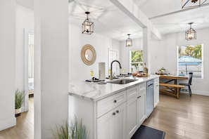 A modern kitchen with white cabinetry, a marble countertop, a sink, and pendant lighting.