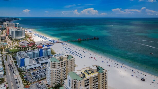 A coastal cityscape with a beach, high-rise buildings, and a pier extending into the ocean.