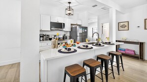 A modern kitchen with white cabinetry, a central island with stools, and a dining area with a view.