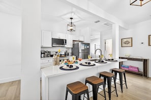 A modern kitchen with white cabinetry, a central island with stools, and a dining area with a view.