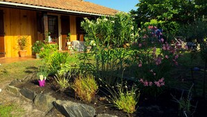 A wooden house with a tiled roof, a garden with various plants and flowers, and a clear blue sky. - Family home between lake, ocean and Bassin d'Arcachon (La Teste-de-Buch)