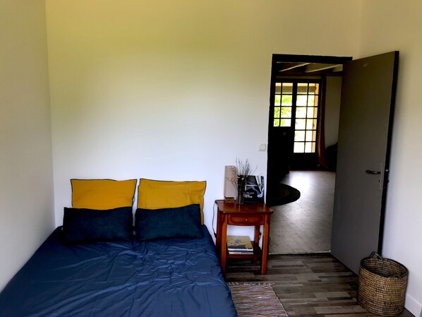 Un dormitorio con cama, mesita de noche, una alfombra pequeña y una puerta que da a otra habitación.