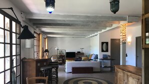 A spacious living area with a wooden dining table, a sofa, and a TV. There are multiple windows and a staircase leading to another level. - Family home between lake, ocean and Bassin d'Arcachon (La Teste-de-Buch)