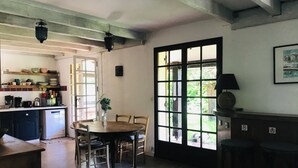 A kitchen with wooden cabinets, a dining table with chairs, a hanging light fixture, and a large window with a view of greenery. - Family home between lake, ocean and Bassin d'Arcachon (La Teste-de-Buch)