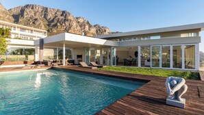 A modern house with a swimming pool, outdoor seating, and a view of mountains.
