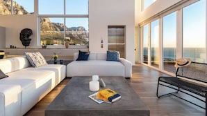 A modern living room with a large window, a sofa, a coffee table with books, and a view of the ocean.