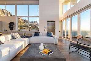 A modern living room with a large window, a sofa, a coffee table with books, and a view of the ocean.