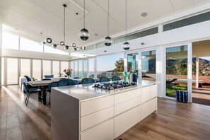 A modern kitchen with a central island, large windows, and a view of the outdoors. - Thabisa Penthouse Supreme Views & Exquisite Design (Cape Town)
