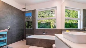 A modern bathroom with a large bathtub, a double sink vanity, and a window providing a view of greenery.