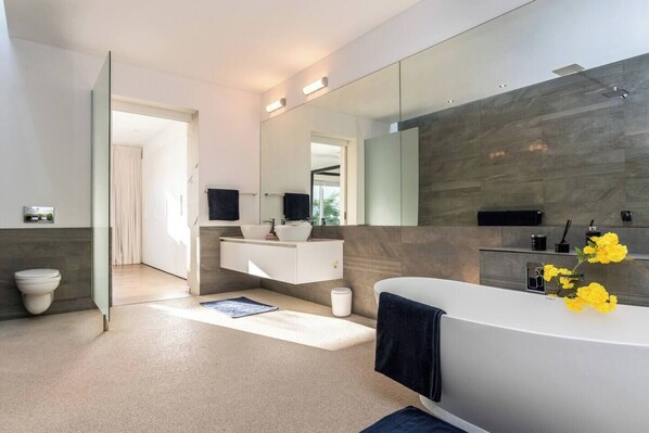 A modern bathroom with a large bathtub, a vanity with a mirror, and a toilet.
