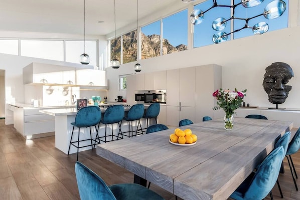 A modern kitchen with a central island, bar stools, and a dining table with a fruit bowl.
