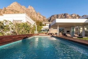 A swimming pool with a wooden deck, lounge chairs, and a mountain backdrop. - Thabisa Penthouse Supreme Views & Exquisite Design (Cape Town)