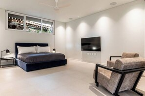 A modern bedroom with a bed, a TV, a chair, and a window with a view of a construction site.