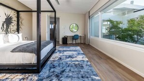 A bedroom with a four-poster bed, a large window, and a view of greenery outside.
