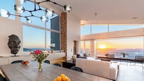 A modern interior with a dining area, a large window with a sunset view, and a decorative wall.